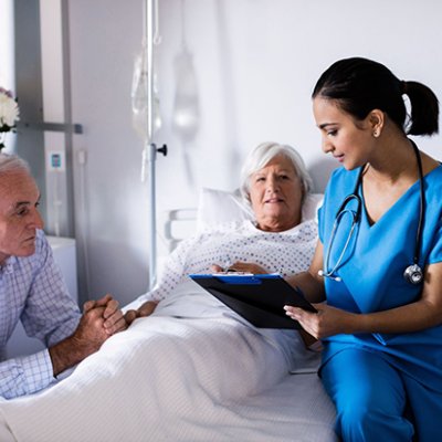 A woman in a hospital bed with a man sitting bedside and a doctor sitting on the bed.